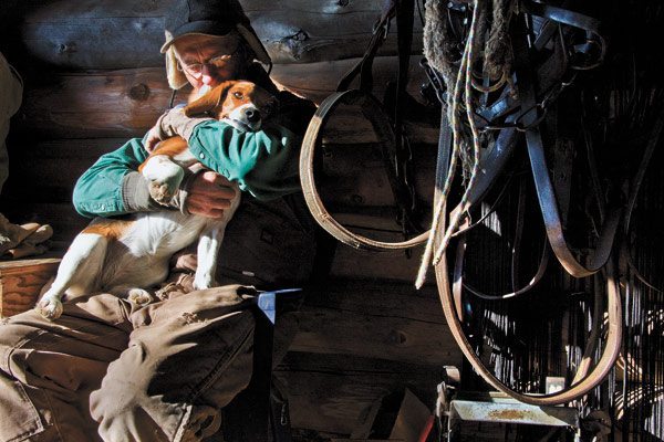 Surrounded by horse tack, Lucy, a two-year-old Beagle, receives a hug from Dave Elliott after morning chores were completed at the family ranch northeast of Maple Creek, Sask. (WP photo by William DeKay)