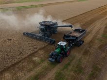 An overhead drone photo showing an autonomous tractor pulling a grain cart receiving grain via a combine's auger in a field, on the fly.