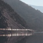 A grain train passes alongside a lake in the mountains.