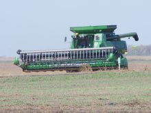 A green John Deere combine is driving down a road during harvest.