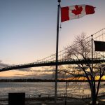 The Ambassador Bridge at sunset with a Canadian flag in the foreground.