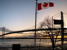 The Ambassador Bridge at sunset with a Canadian flag in the foreground.
