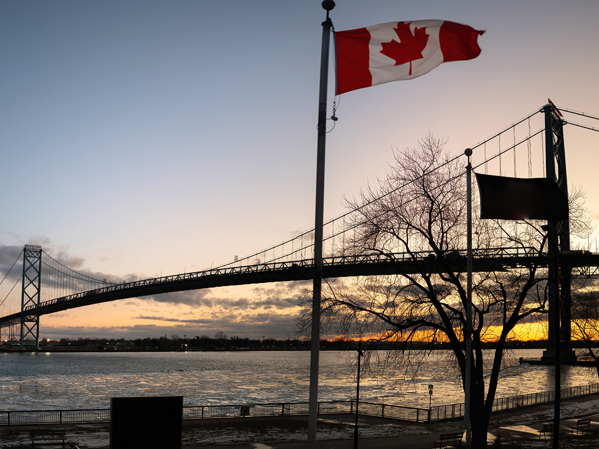 The Ambassador Bridge at sunset with a Canadian flag in the foreground.