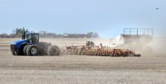 A large blue tractor with eight tires pulls a large air seeder during spring seeding.