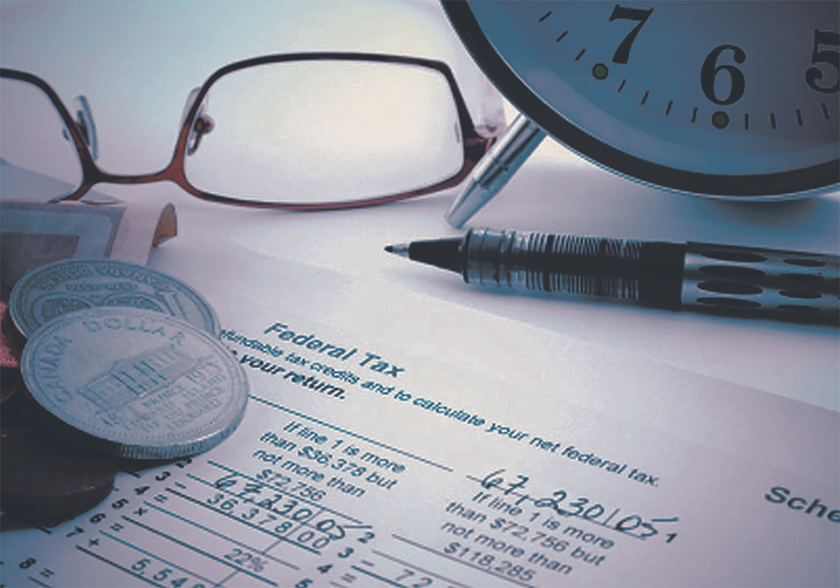 Close-up of glasses, change, a pen and an alarm clock on top of some tax forms on a table.
