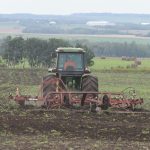 A tractor pulls a cultivator in a field.