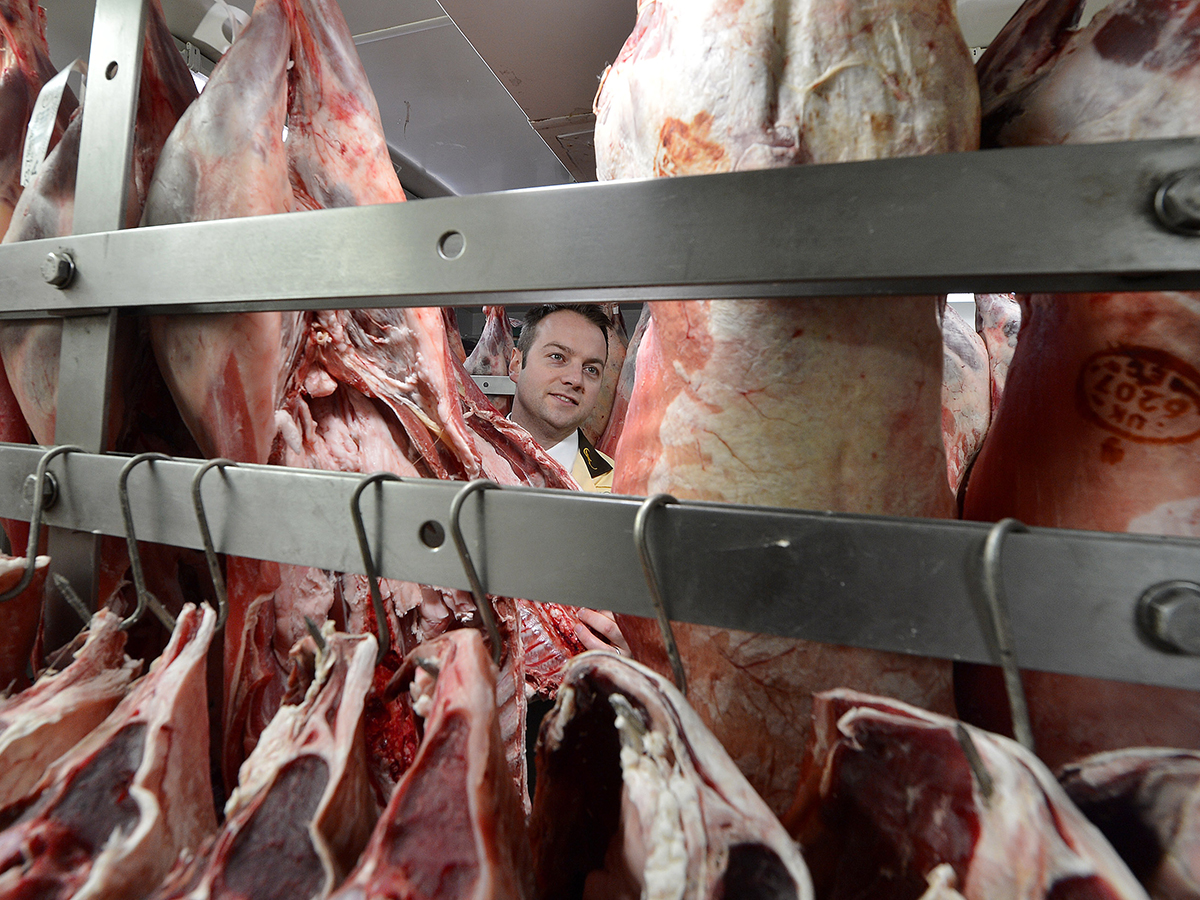 Raw meat hanging on rails in a butcher shop.