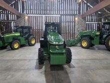 A promotional photo of three new John Deere electric tractors on a stage designed to look like an old barn.