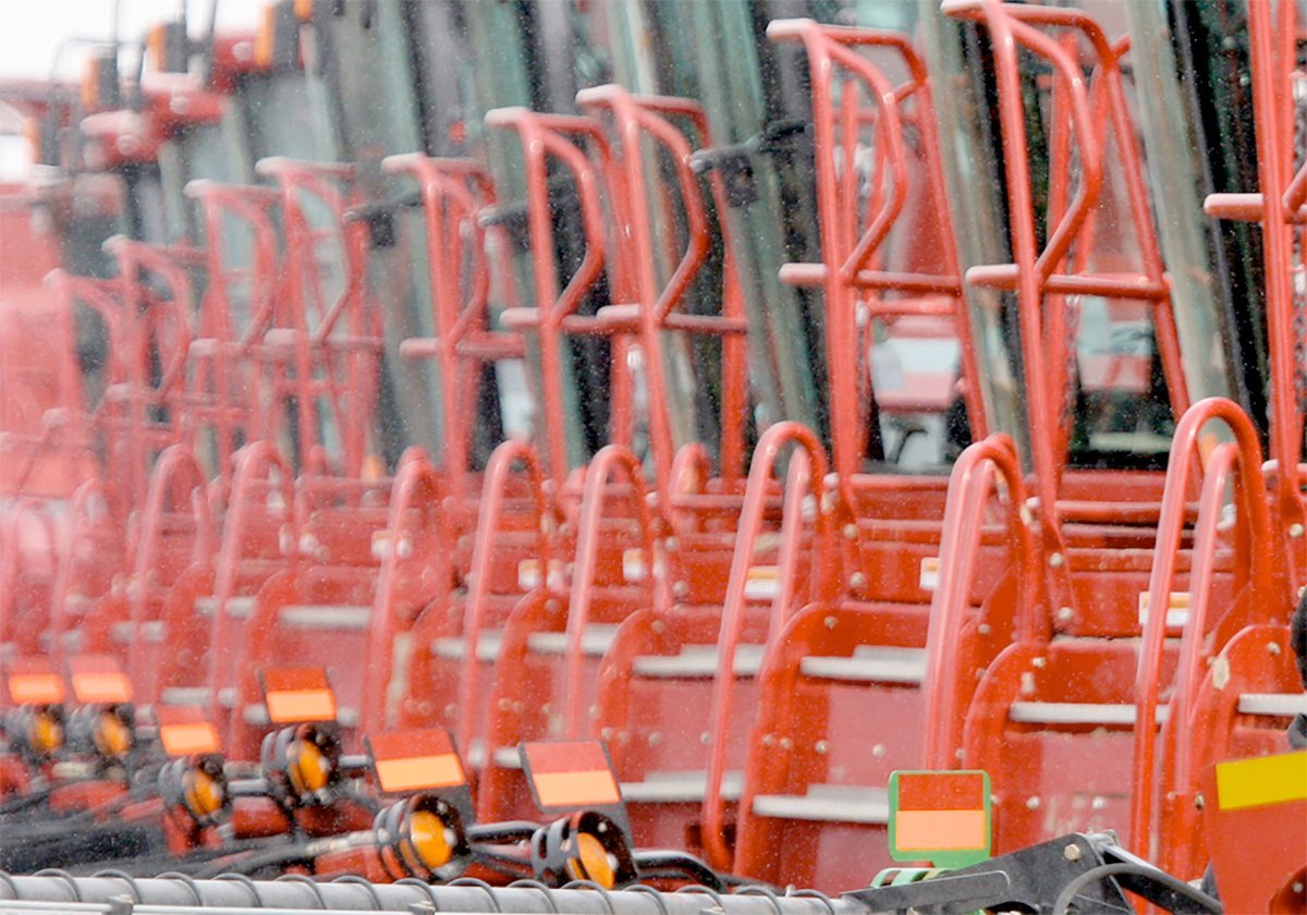 A row of identical red pieces of farm equipment on a dealer's lot.