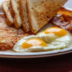 Eggs, sunny-side-up, on a plate with hash browns, bacon and toast.