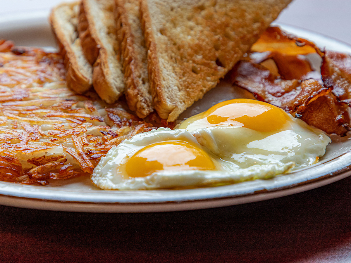 Eggs, sunny-side-up, on a plate with hash browns, bacon and toast.