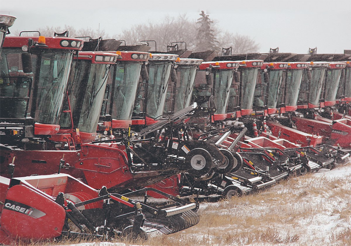 A row of new red combines sit in a field.