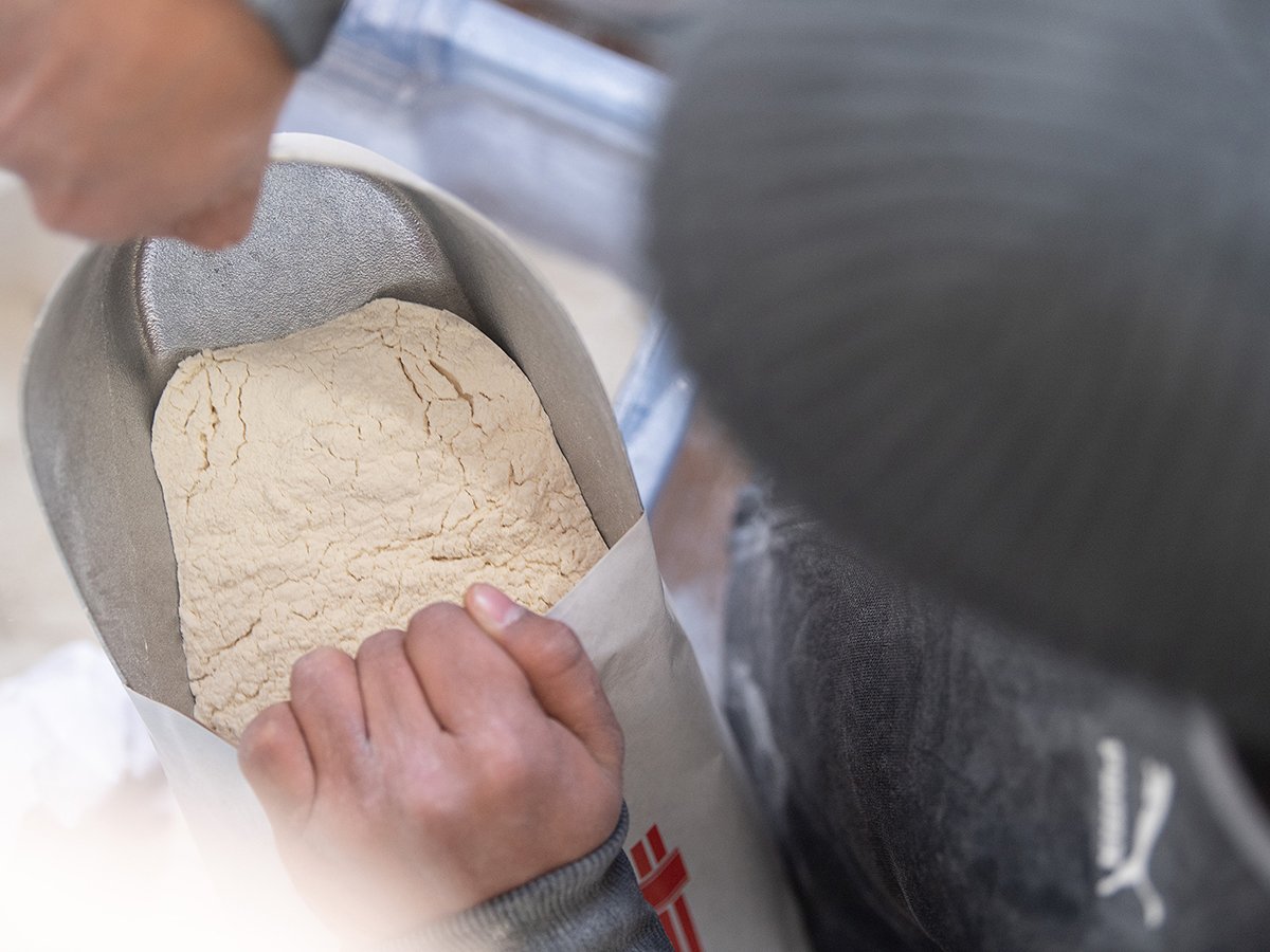 An overhead shot of someone scooping flour out of a paper bag.