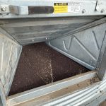 Canola seed is visible through the auger door of a steel bin.