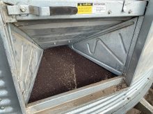 Canola seed is visible through the auger door of a steel bin.
