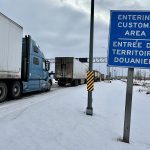 Trucks are lined up on a highway next to a sign that reads, "Entering Customs Area."