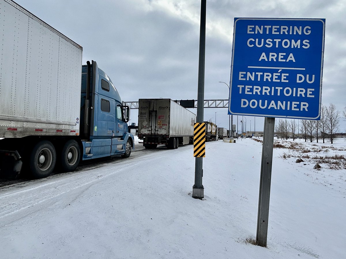 Trucks are lined up on a highway next to a sign that reads, "Entering Customs Area."