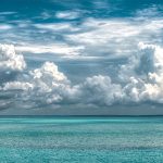 Looking out to sea over a tropical ocean with billowing white clouds in the sky.