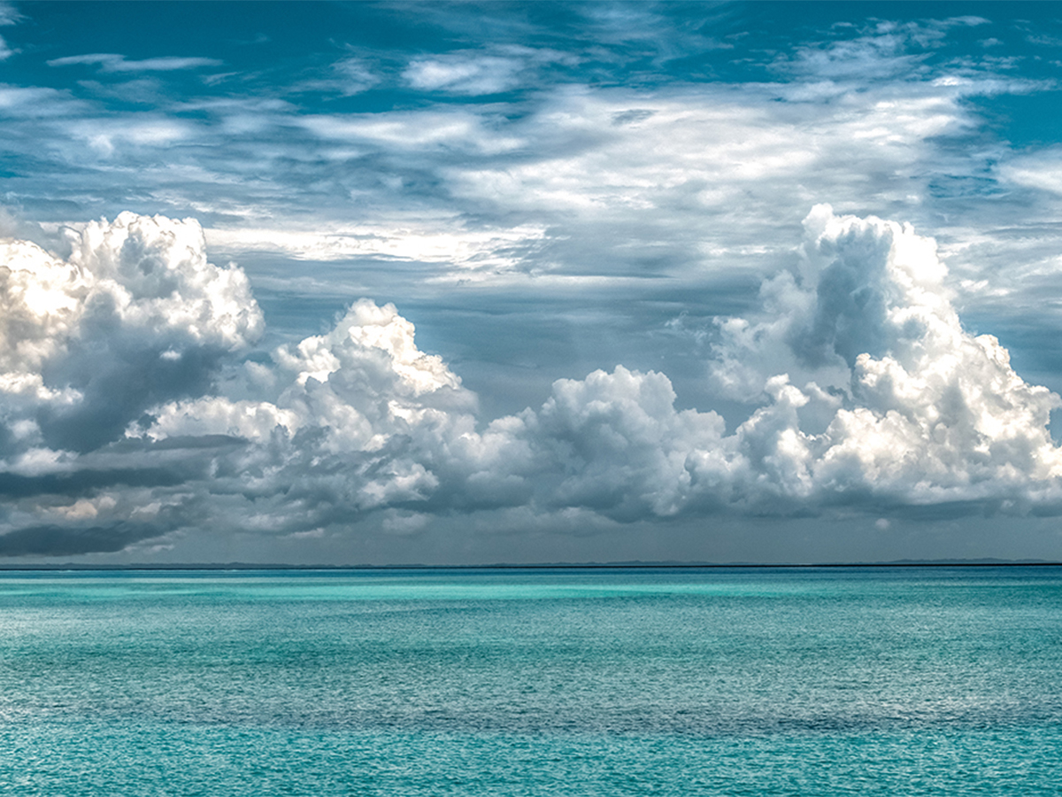 Looking out to sea over a tropical ocean with billowing white clouds in the sky.