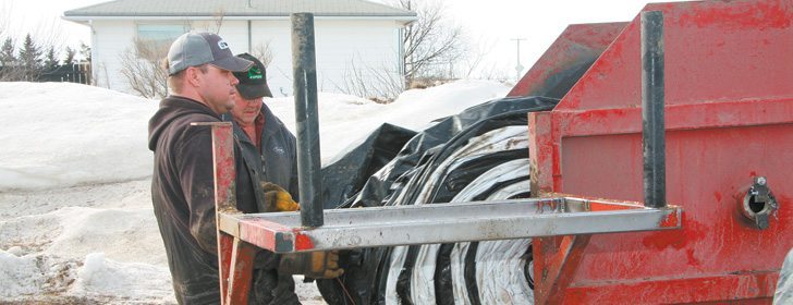 Jeff Brown, foreground, and Bill Brown help the last of a grainbag  through a roller they designed. The pair was shipping their bags to Merlin Plastics in Alberta for recycling. | File photo