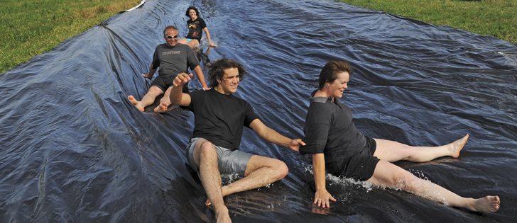 Travis, left, Nicole, Dylan and Dawn Kennedy of Luseland, Sask., take a break from the day’s chores to cool down and enjoy a ride on their homemade water slide made from recycled grain bags.  |  William DeKay photo 