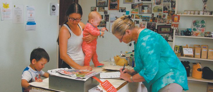 Natasha Pospisil, centre, watches her son, Reese, and holds seven-month-old Tegan while serving area rancher Wendy Carpentier, a regular at the store who says she relies on its post office. |  Karen Morrison photo