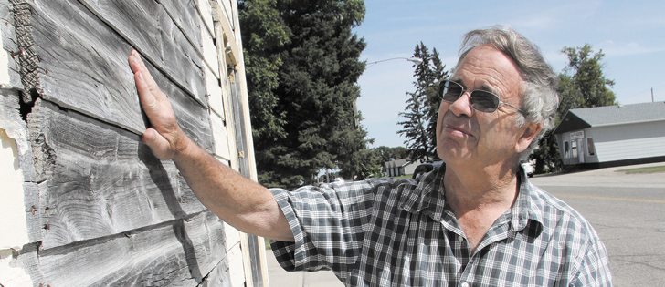 Rick Truelove, a long-time resident of Cypress River, Man., checks out the weathered wood on a building that’s been boarded up for decades. However, a surprising number of businesses are still open on Cypress River’s main street, including a Credit Union and grocery store. |  Robert Arnason photo