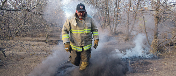 Pete Neudorf, a volunteer fire fighter from the Burstall, Sask., fire department, stamps out stubborn hot spots in a shelterbelt southwest of the community, Oct. 18.  |  William DeKay photo