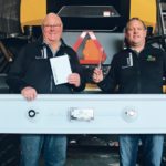 Pat, left, and Trevor Scherman hold the ScherGain drop pan. The round steel electromagnets are visible on each side of the pan. Trevor holds the grain gauge and Pat holds the chart operator’s reference to understand the losses. | ScherGain photo