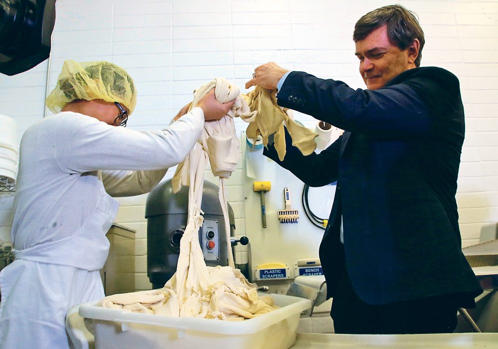 Skeena Ngo, a research and development assistant at Crust Craft, and Alberta Agriculture Minister Oneil Carlier transfer dough to a mixer. Crust Craft has taken part in the government’s energy efficiency grant program. |  Jeremy Simes photo
