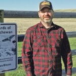Merek Wigness stands in front of one of the stewardship program signs installed on his farm. | Submitted photo