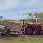 Carson Ebeling, 14, drives a 1950 McCormick Super W6 tractor to seed barley from his 1929 John Deere steel wheel seed drill. | Maria Johnson photo