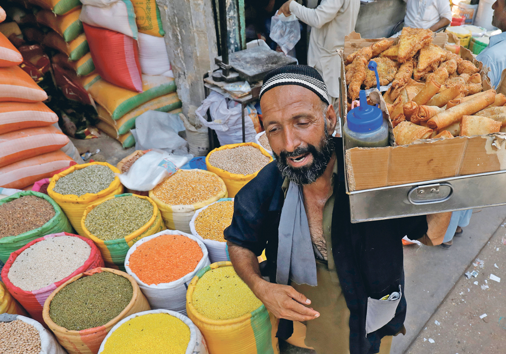 A vendor with a pane of vegetable rolls and samosas, a traditional snack, walks past the sacks of grain and lentils at wholesale market in Karachi, Pakistan, April 2. It once bought 15 percent as much of Canadian pulses as India, now it buys 50 percent due to its neighbour’s reduced purchases. | REUTERS/Akhtar Soomro photo