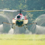 There is a common misconception that helicopter rotors push the spray down toward the crop. However, as this photo of a Yamaha R-Max shows, the down-wash sends product swirling in all directions. Spraying expert Tom Wolf says this is a major factor that may prevent rotary drones from receiving federal approval for spraying. | Creative Commons image