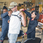 Abisola Omoniyi and Ornwipa Thamsuwan from the Canadian Centre for Health and Safety in Agriculture at the University of Saskatchewan hook an exoskeleton to Ron Swan of Glenside, Sask., who volunteered to test the unit on the farm. | William DeKay photo