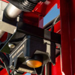 The orange-colored Raven sensor pointing down is one of five sensors measuring ground speed and distance from the soil or crop canopy. The CNH plug at the top of the photo is the Aim Command Flex Nozzle control valve that controls the spray tip. | Raven photo