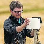 Blake Weiseth investigates a Metos rain gauge connected to an in-ground soil moisture probe which will be used to measure water infiltration rates and soil-water dynamics in the pothole consolidation project at the Discovery Farm near Langham, Sask. | Glacier FarmMedia Discovery Farm photo