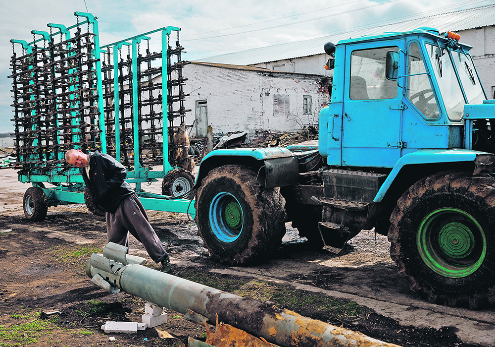 A farm worker at a tractor yard in the village of Yakovlivka outside Kharkiv, Ukraine, looks at a rocket that had landed in a field earlier this month after it was hit by an aerial bombardment.  |  Reuters/Thomas Peter photo