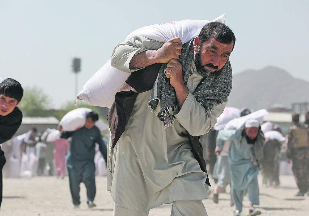 Many countries cut aid to Afghanistan following the fall of Kabul to halt the flow of money to the Taliban, which is considered a terrorist organization. However, the authors say this decision has caused suffering for innocent Afghans in the midst of a humanitarian crisis of massive proportions.  These men carry sacks of rice that were part of humanitarian aid sent by China in April.  |  Reuters/Ali Khara photo