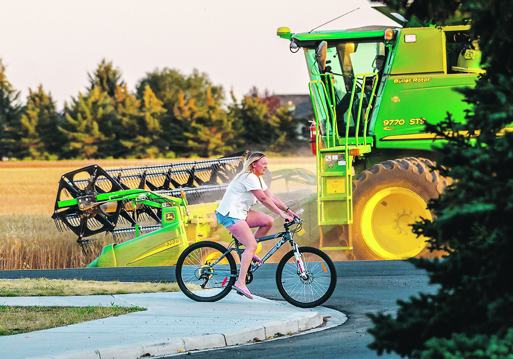 A cyclist rides on the outer edge of High River, Alta., as Cristy Monteith combines a wheat crop across the street. Crops across the Prairies are highly variable due to some odd moisture timing and, in some cases, patchy drought this year. High River has had about 95 percent of its average rainfall, but areas such as the Peace River district are at 75 percent and in the southwest only 65 percent has fallen. In Saskatchewan it ranges from 135 percent in the southeast and northwest to 75 in the southwest. While Manitoba saw near normal in the northwest to double that in the southeast.  |  Mike Sturk photo.