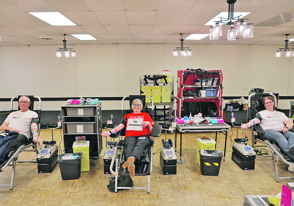 Les Trautman of Camrose, left, and Margaret Shinness of Wetaskiwin, Alta., right, join their sister, Virginia Liebl of Camrose, to help celebrate her 100th donation Feb. 20 at the travelling Canadian Blood Services donation centre in Camrose on Family Day.  |  Mary MacArthur photo