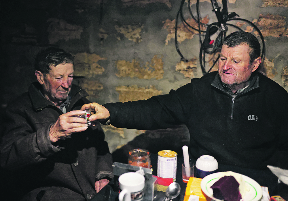 Stepan Kovalyov, 80, and his brother, Volodymyr Kovalyov, 77, toast with horilka, a Ukrainian spirit, inside a cellar where Stepan and his wife live after their house was destroyed during the Russian occupation of their village northwest of Kherson, Ukraine.  |  Reuters/Nacho Doce photo