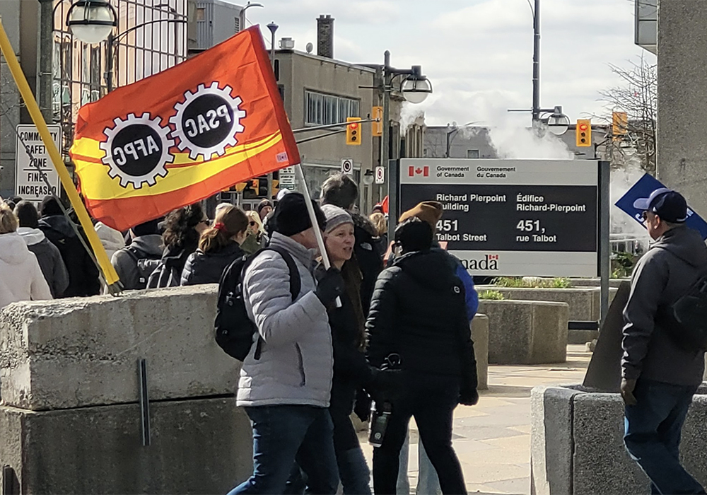 PSAC workers on strike carry a PSAC flag in front of a federal government building in London, Ontario, April 19, 2023.