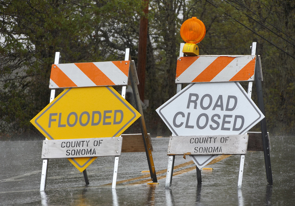 Two signs, one reading "Flooded," and the other reading, "Road Closed" on a wet road somewhere in Sonoma County, California.