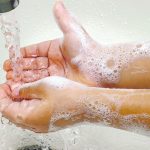 Close-up photo of soapy hands in a sink under running water.
