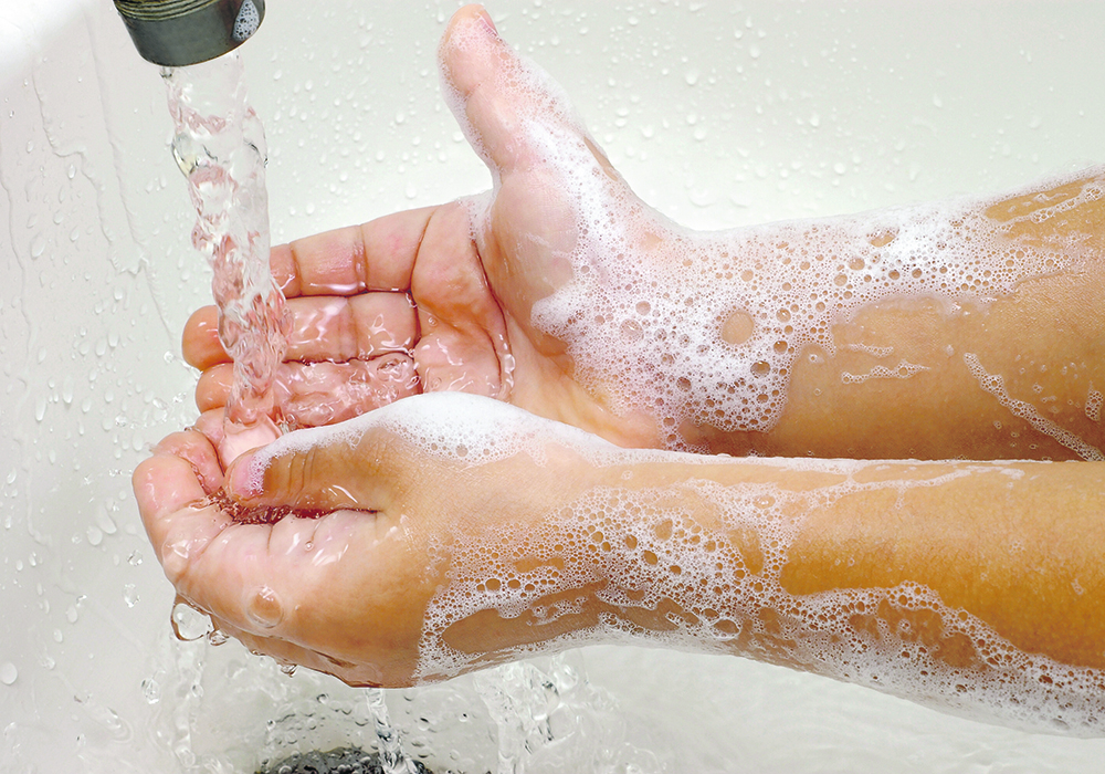 Close-up photo of soapy hands in a sink under running water.