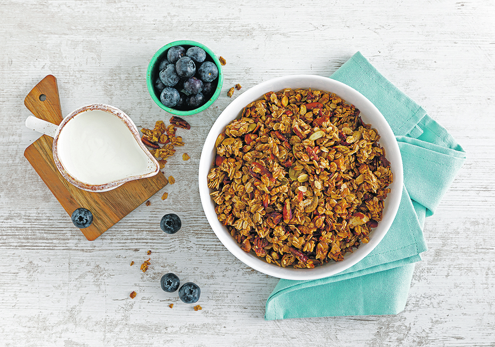 A stock overhead photo of a bowl of granola, a small pitcher of milk, and a small bowl of blueberries.