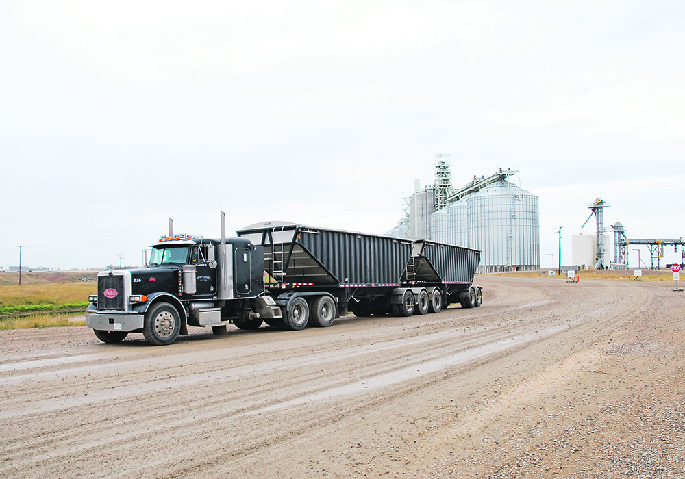 A semi truck pulling a B-train driving away from a large, modern inland grain terminal.