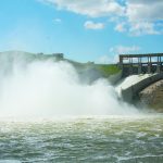 Water sills violently over a dam on the Oldman River in Alberta, putting spray into the air.