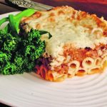 Close-up photo of a piece of Greek pastitsio sitting on a plate with garnish.